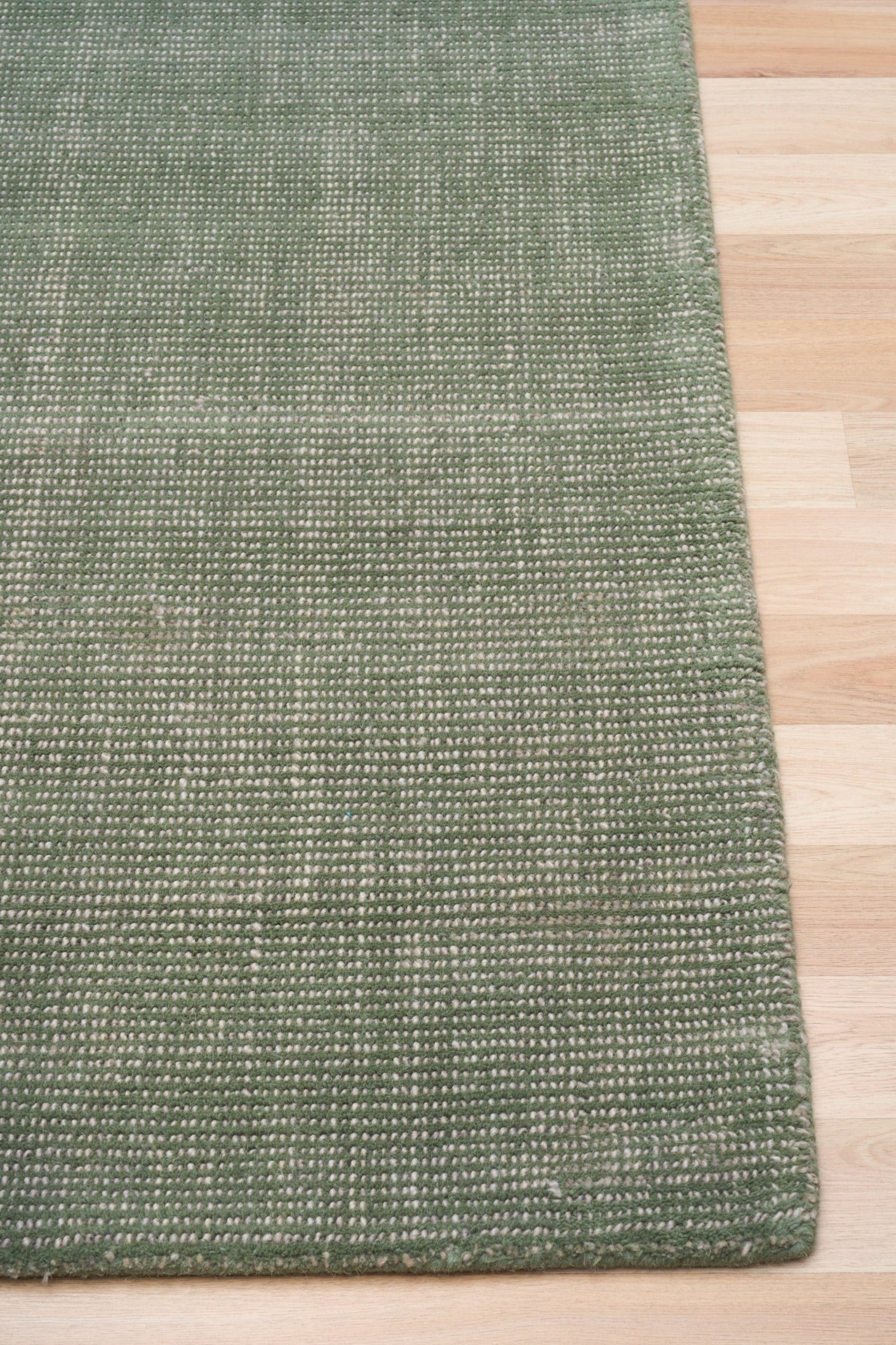 Green area rug with visible hemmed edge on light wood flooring