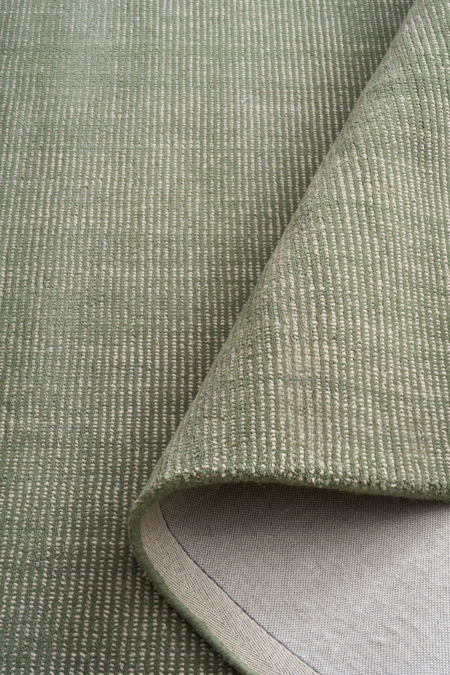 Green area rug fabric close-up with curled edge and light interior backing
