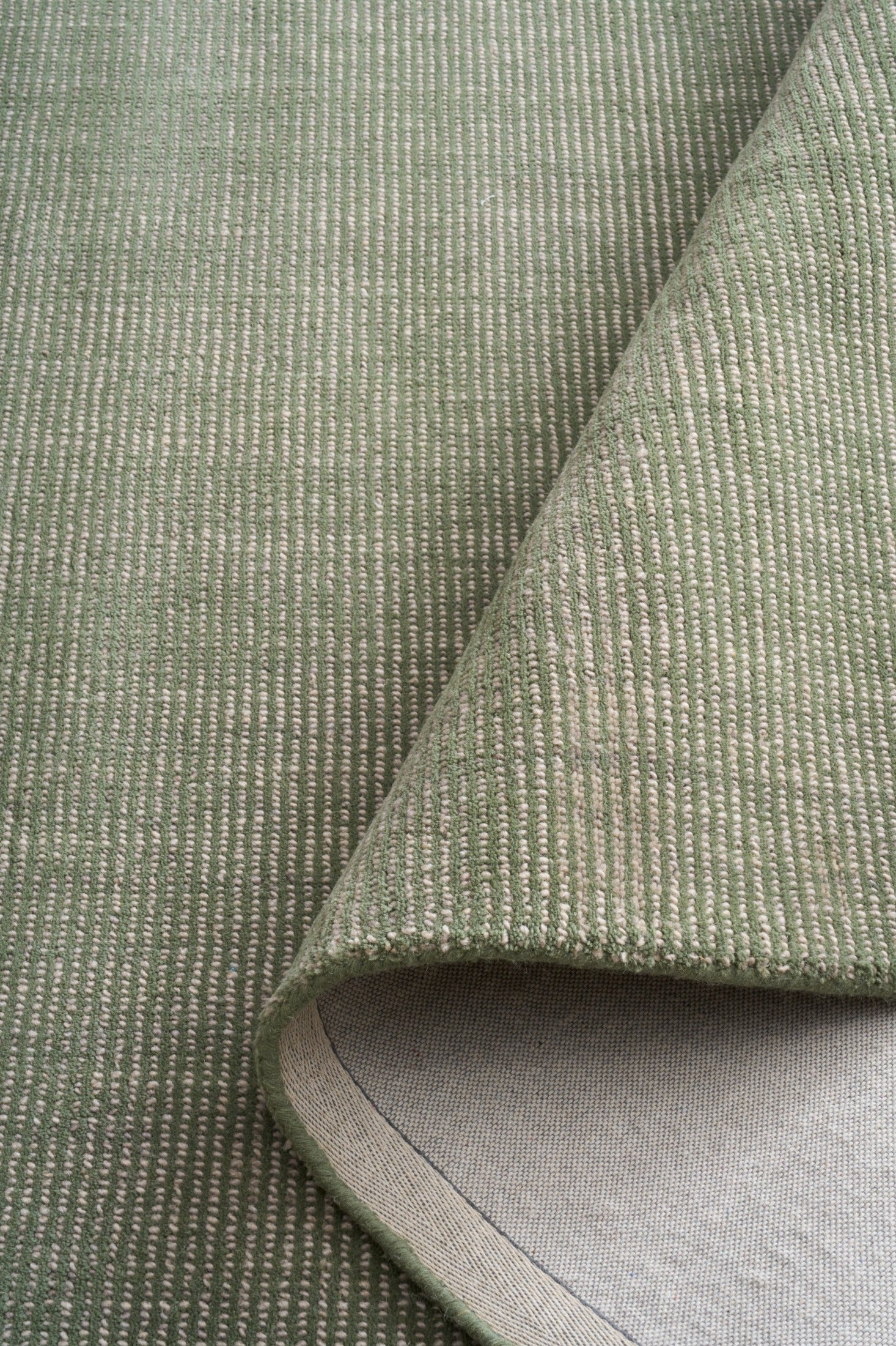 Green area rug fabric close-up with curled edge and light interior backing