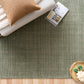 Green area rug with folded blankets and decorative items on top, top-down view