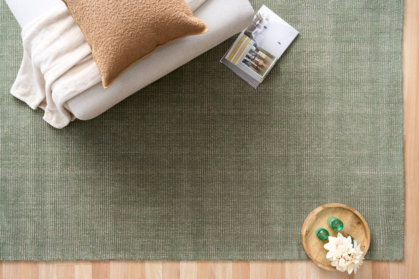 Green area rug with folded blankets and decorative items on top, top-down view