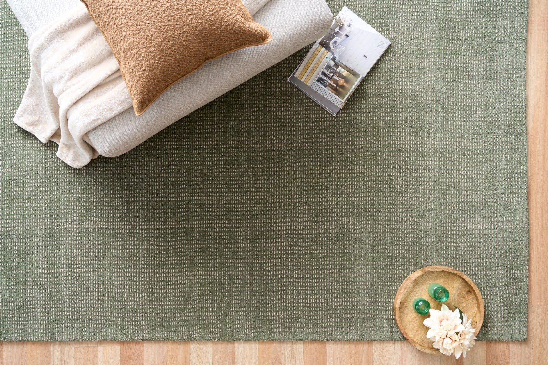 Green area rug with folded blankets and decorative items on top, top-down view