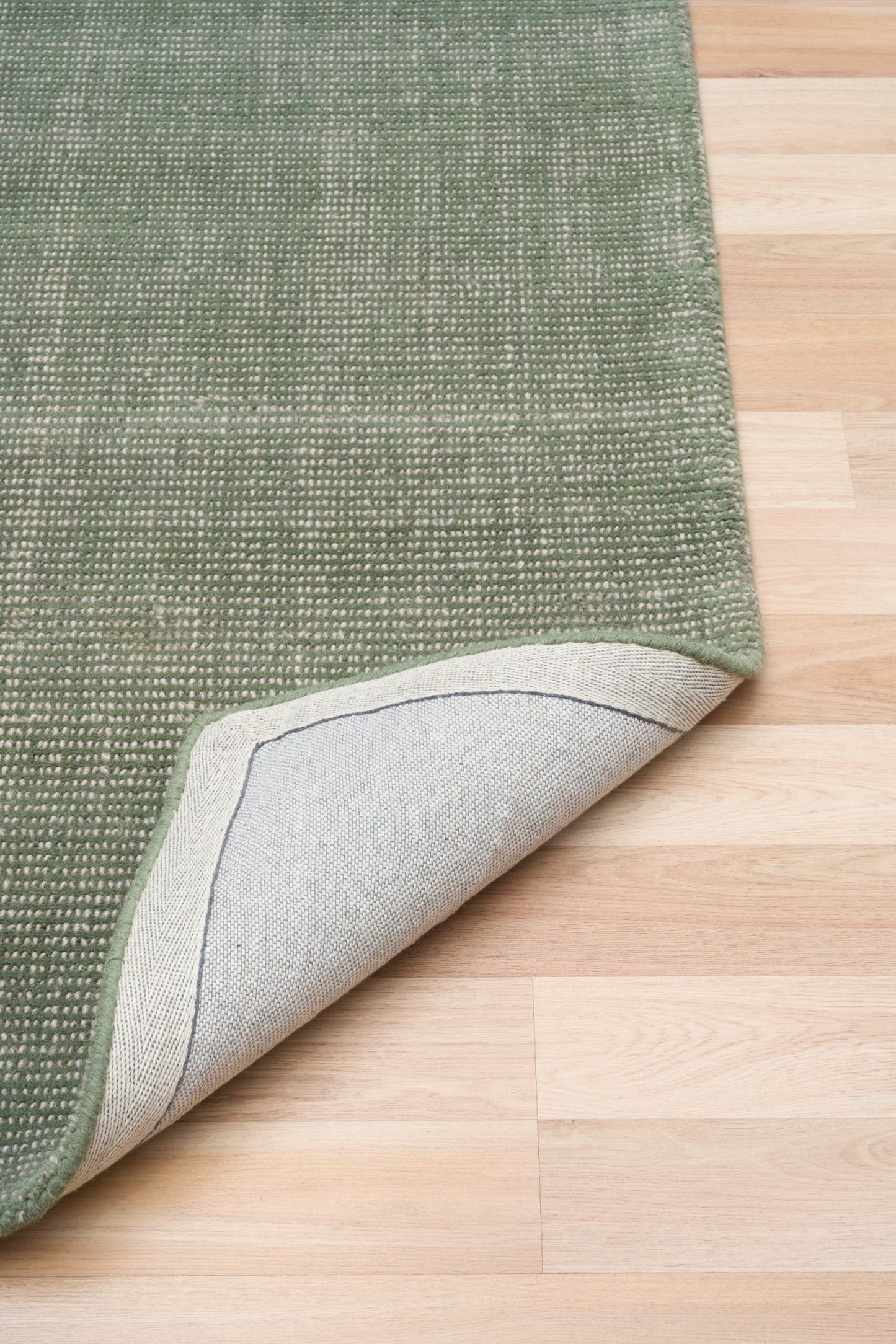 Green area rug corner with stitched edge, rolled back to show the light backing