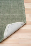 Green area rug corner with stitched edge, rolled back to show the light backing