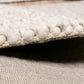 Corner edge of cream wool rug with braided trim and low-profile woven backing