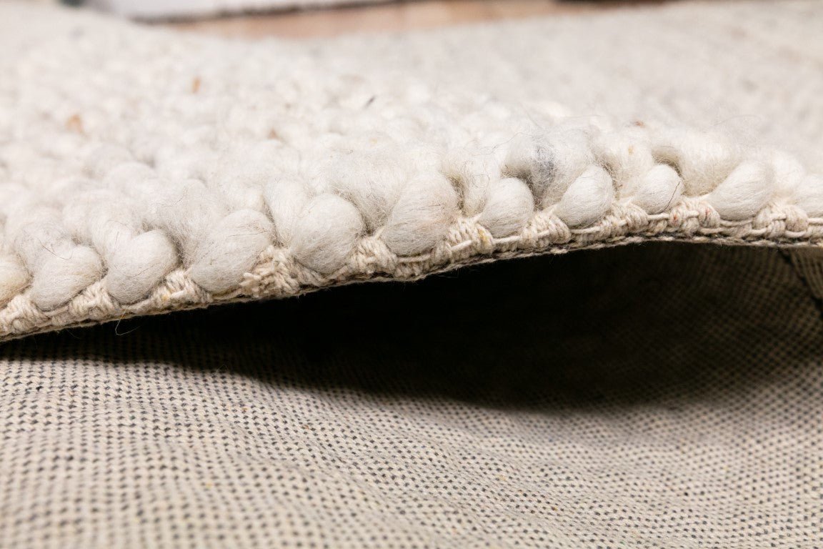 Corner edge of cream wool rug with braided trim and low-profile woven backing