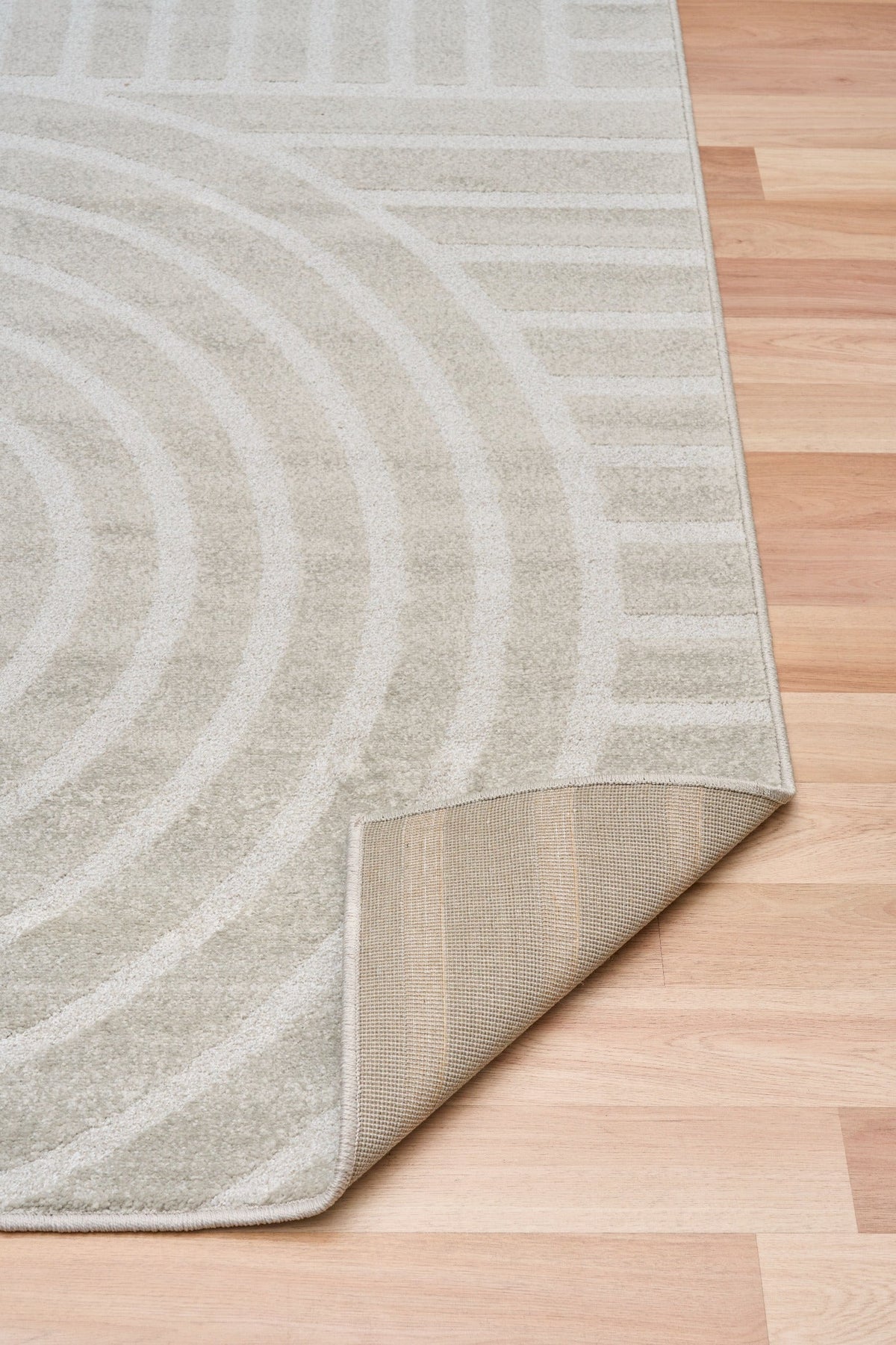 Light gray area rug with abstract arch and stripe motif, angled view of edge