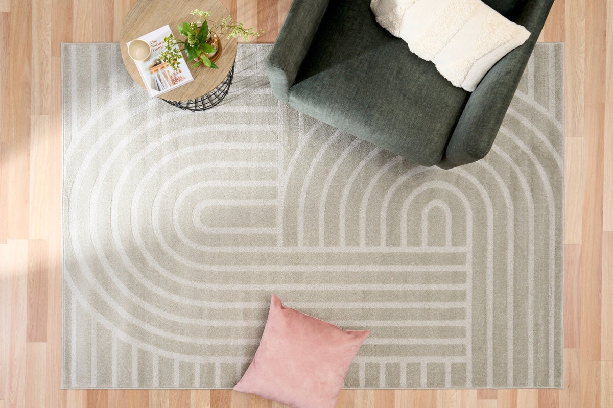 Light gray area rug with abstract arch and bar stripe pattern, corner view with sofa