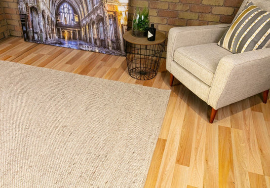 Stone beige wool rug corner with low-pile woven texture on hardwood flooring