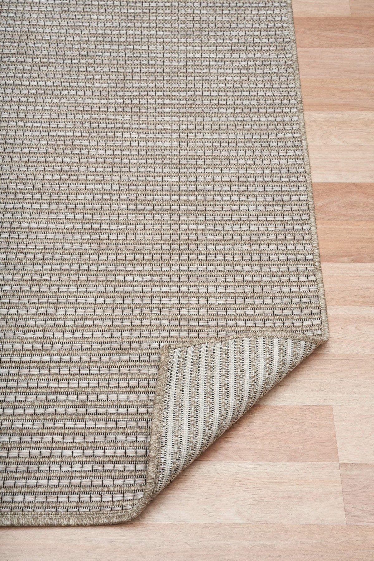 Folded edge of woven outdoor rug with striped border and textured weave