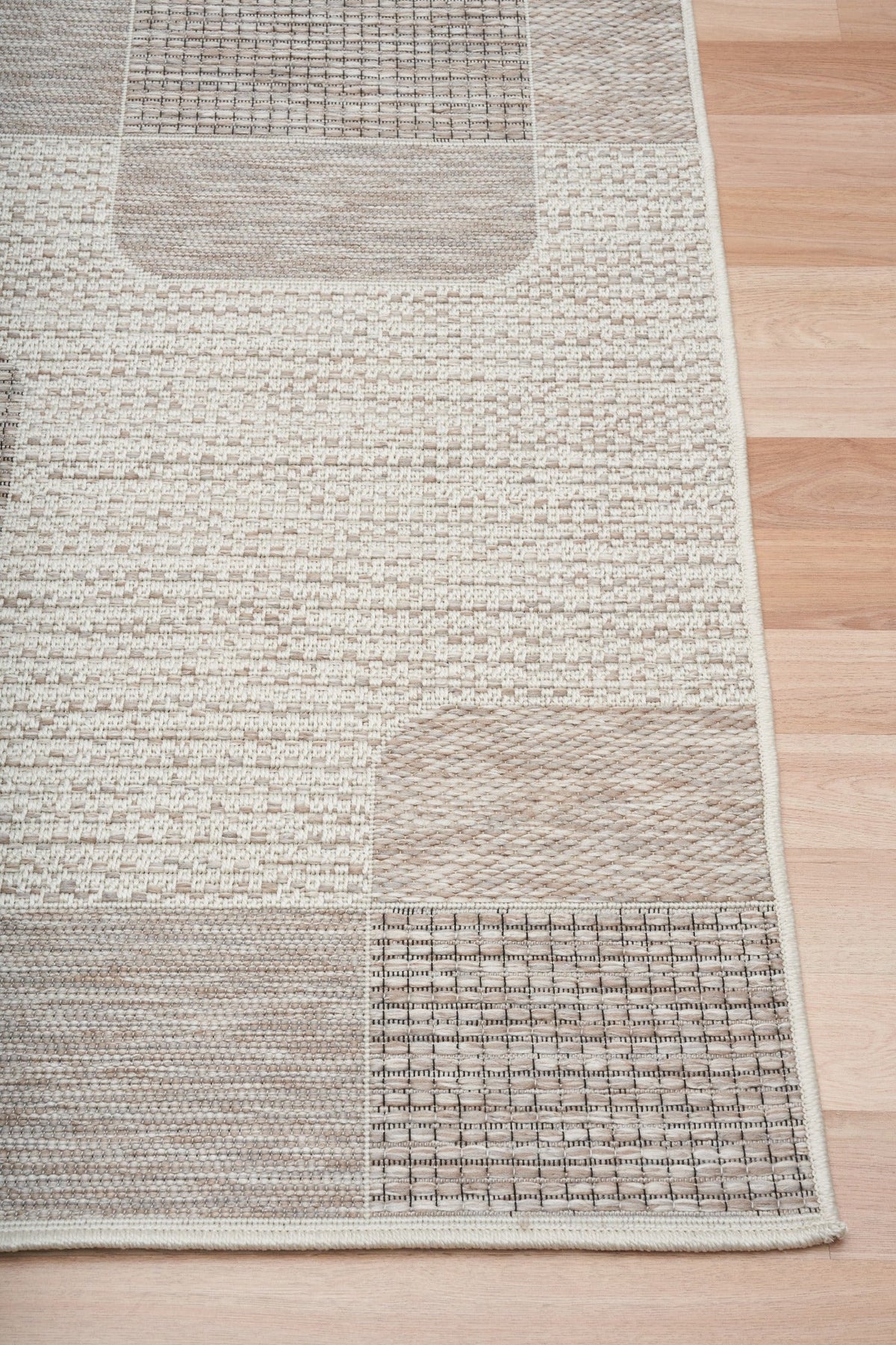 Woven rug corner with beige and taupe patchwork texture and trimmed edge