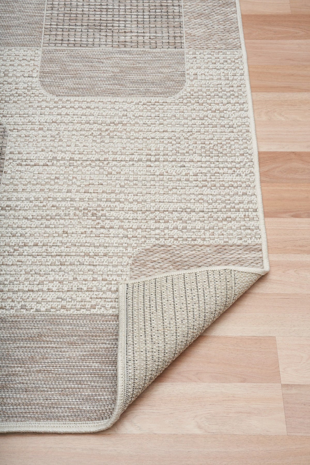 Woven rug with beige-and-taupe patchwork and visible stitched overlock edge