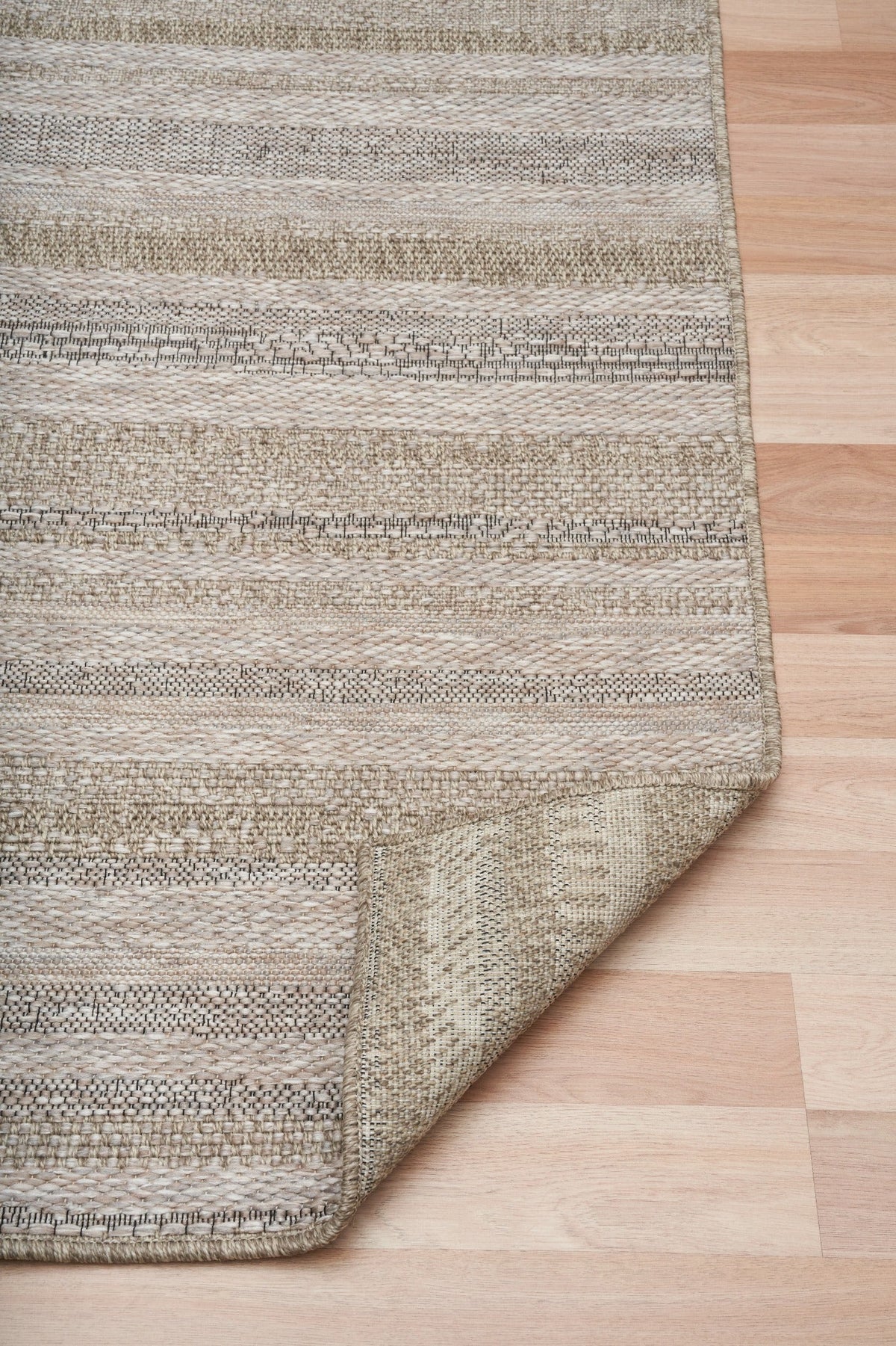 Corner with stitched border of light beige and gray woven striped area rug.