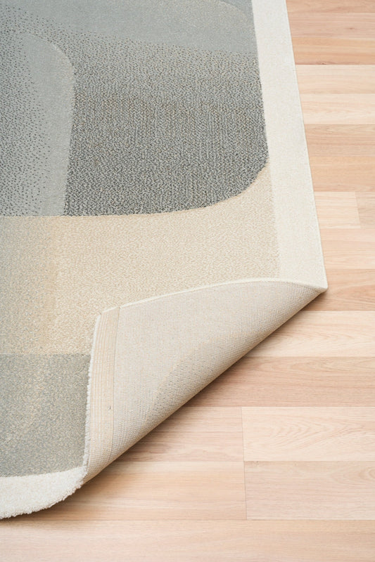 Beige and gray abstract area rug corner with turned-under edge and textured pile