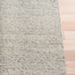 Light grey speckled area rug side view with low profile edge on wood floor