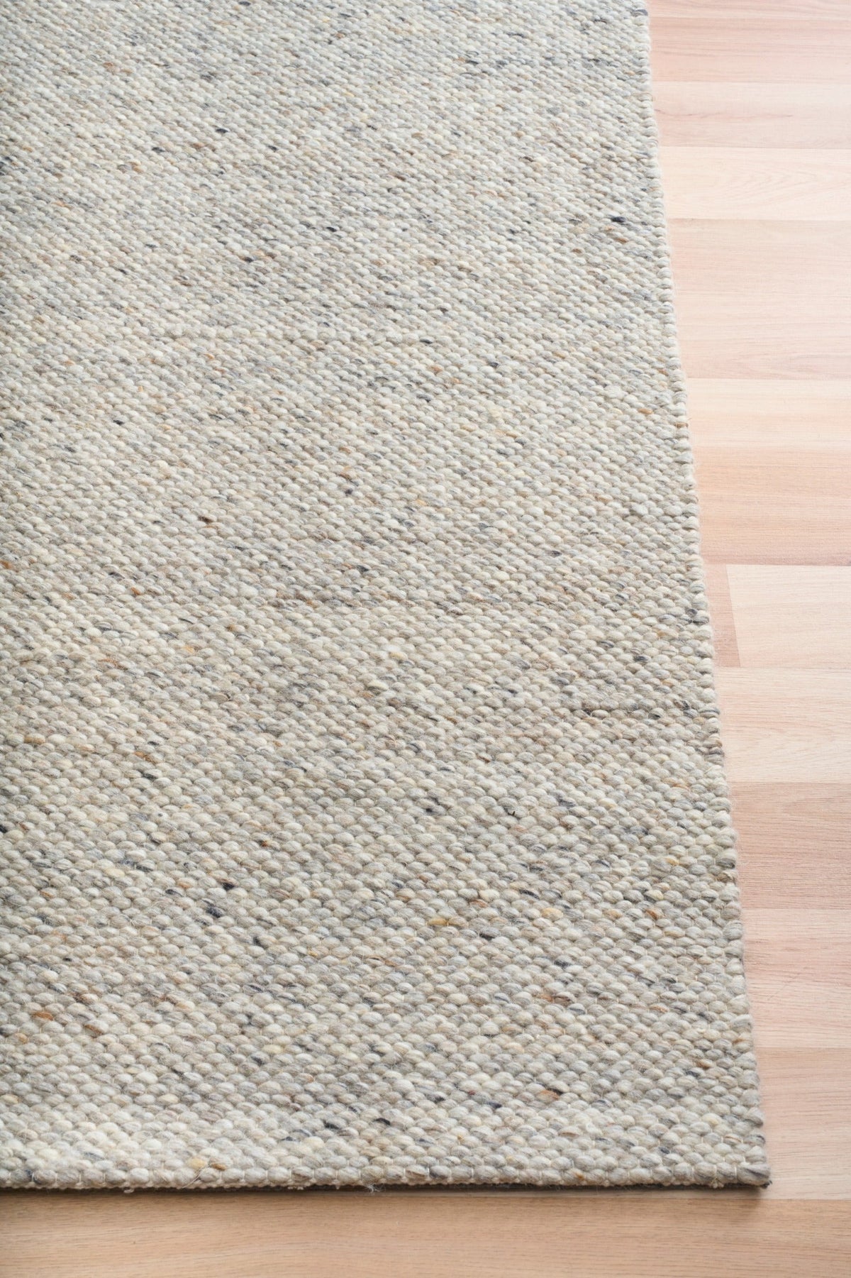 Light grey speckled area rug side view with low profile edge on wood floor