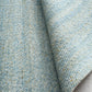 Close-up of light blue rug weave texture with fine speckled fibers and tight pile.