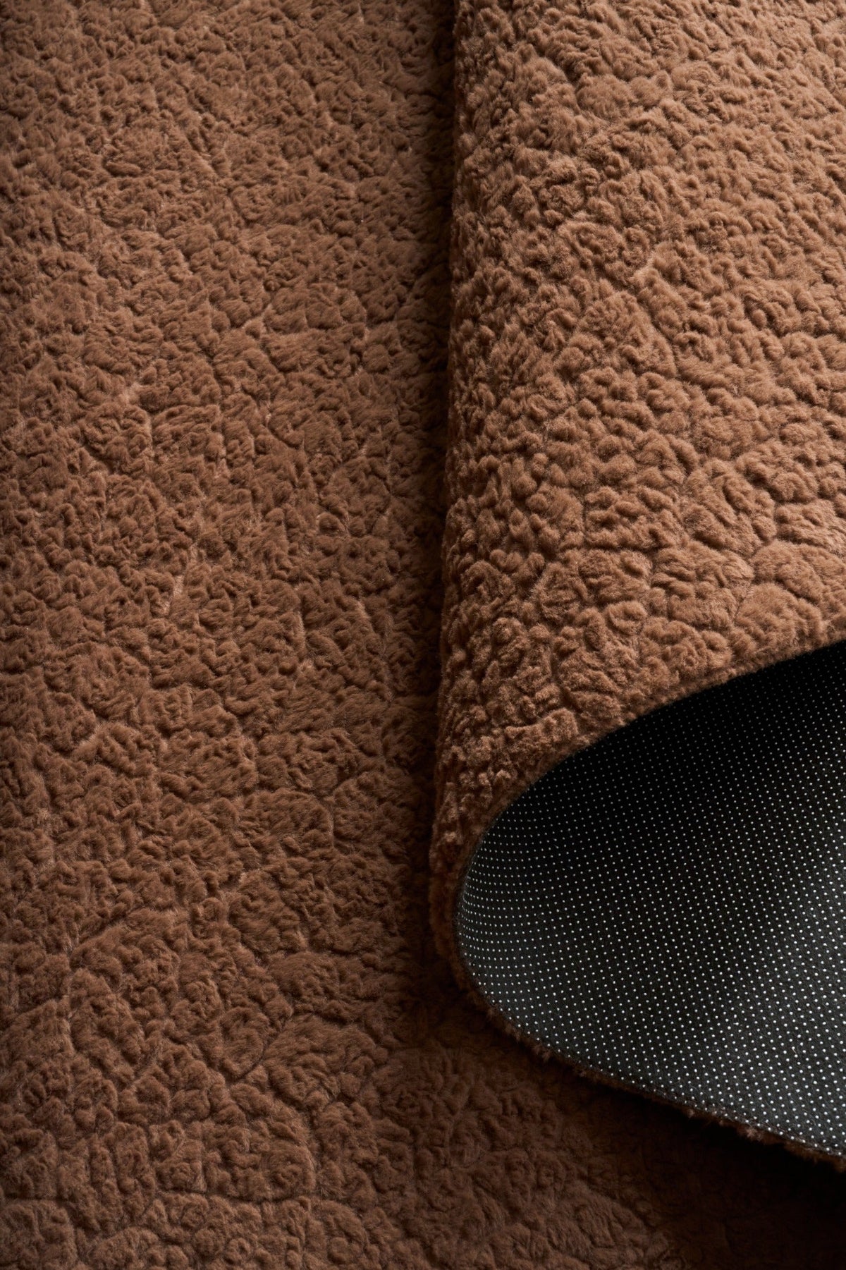 Brown shaggy area rug, thick textured pile with rolled edge and dark underlayer