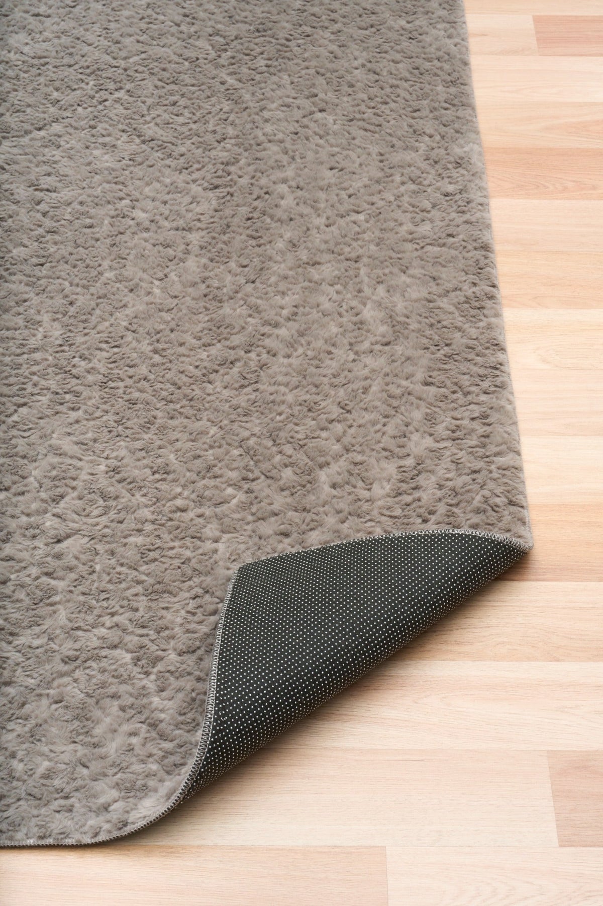Gray shaggy rug corner with dark woven backing underside