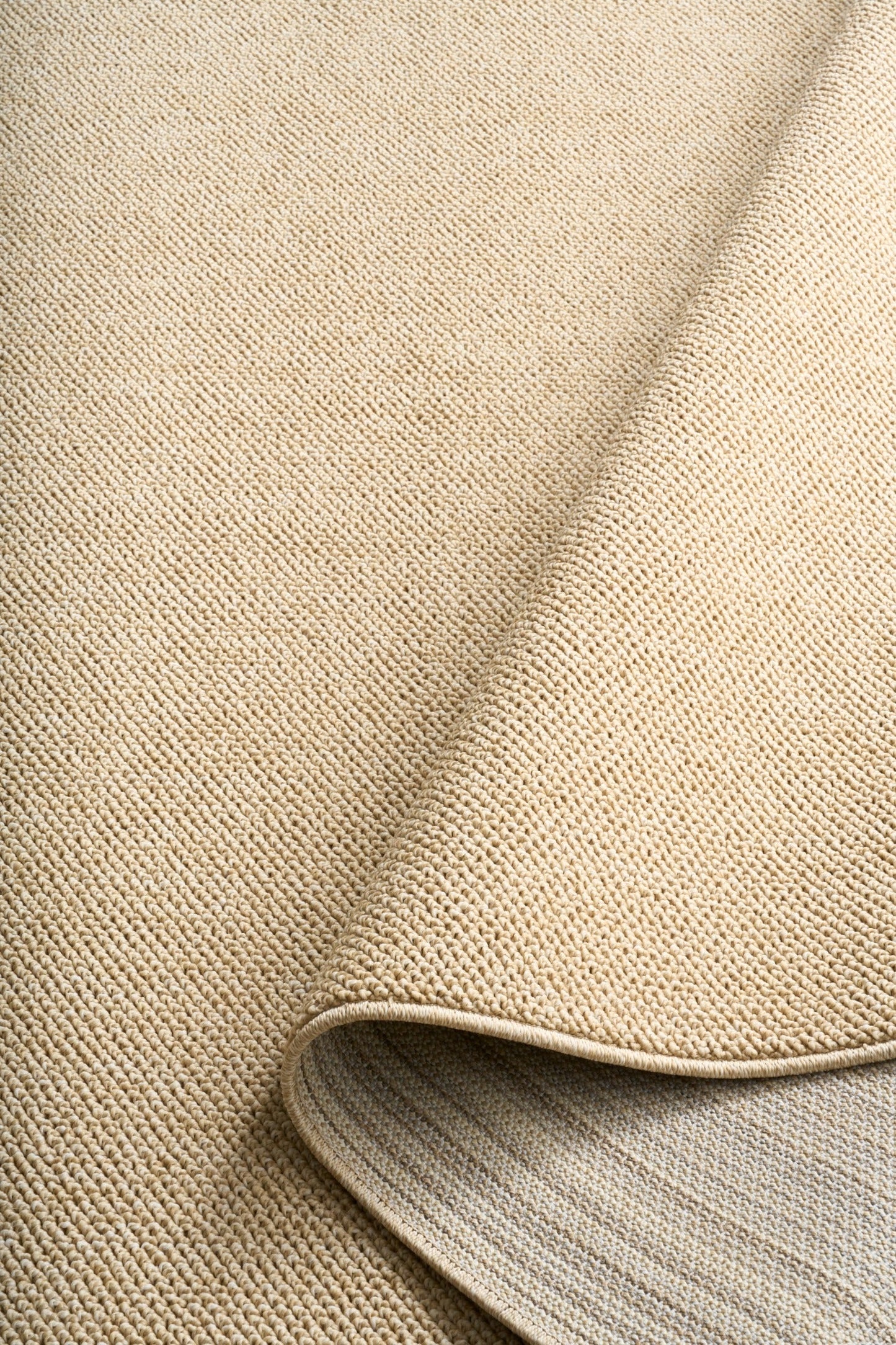 Beige area rug edge with rounded bound trim and close-up weave