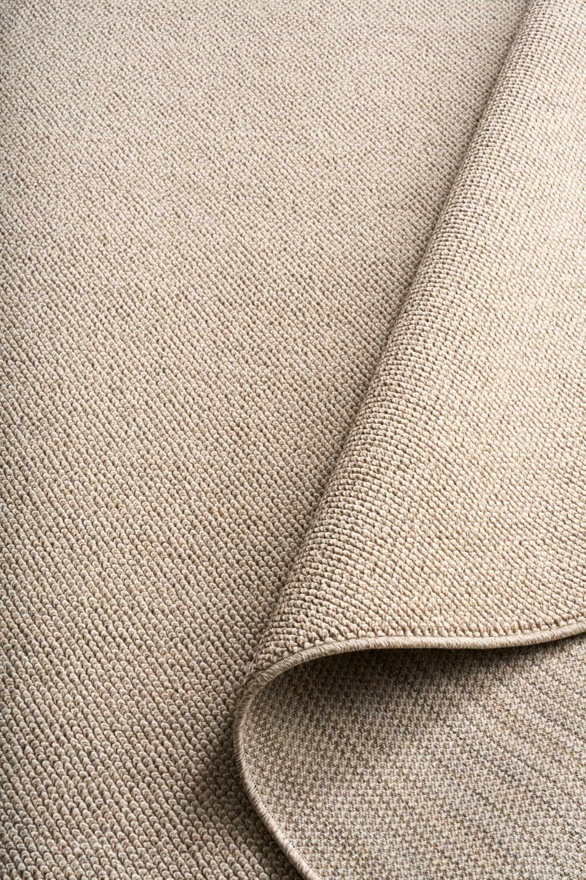 Light brown textured area rug corner with rounded underlayer edge