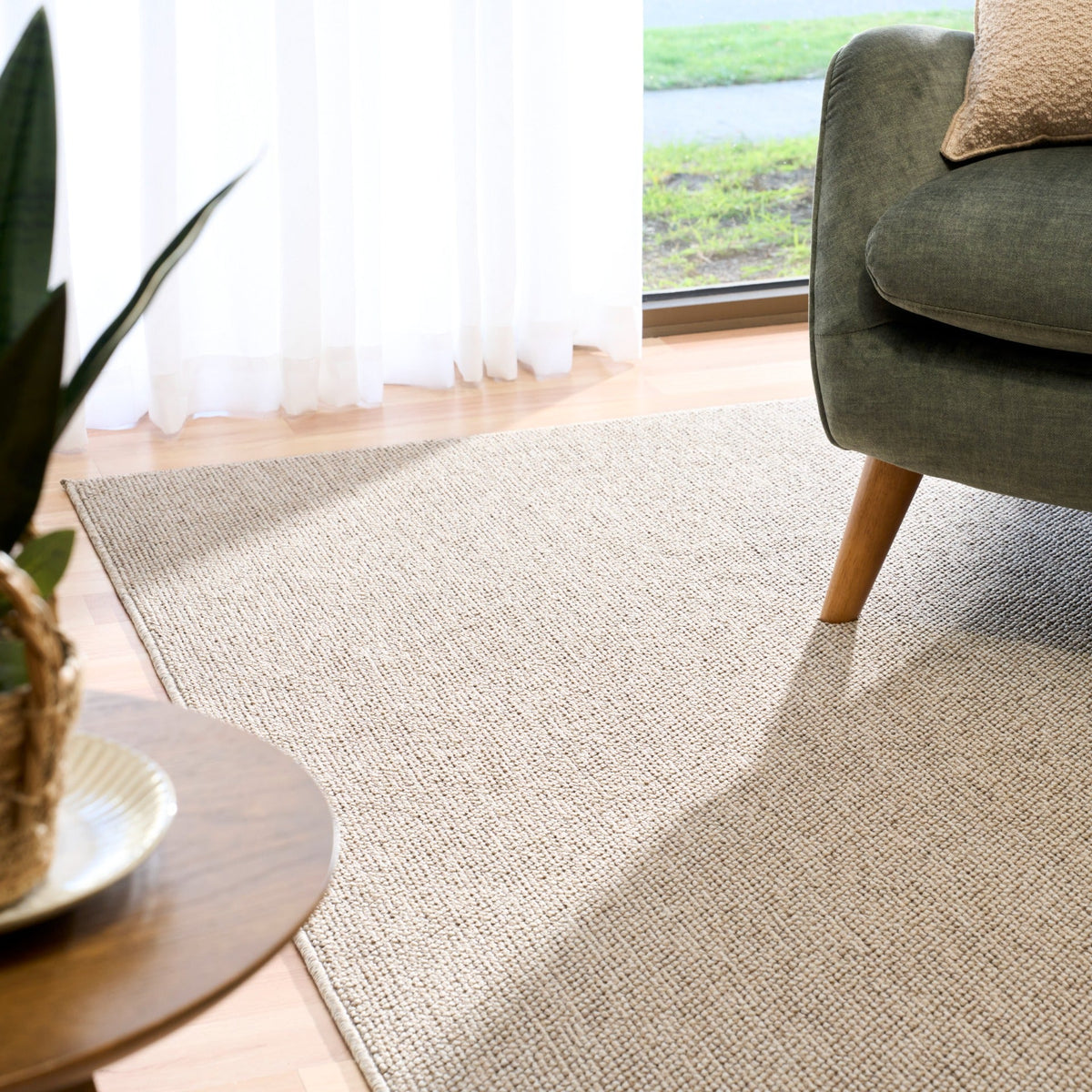 Light brown textured area rug with corner placement and sofa leg visible