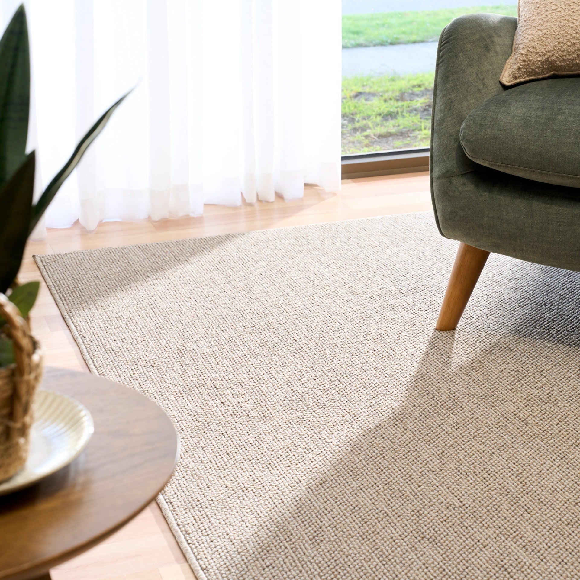 Light brown textured area rug with corner placement and sofa leg visible