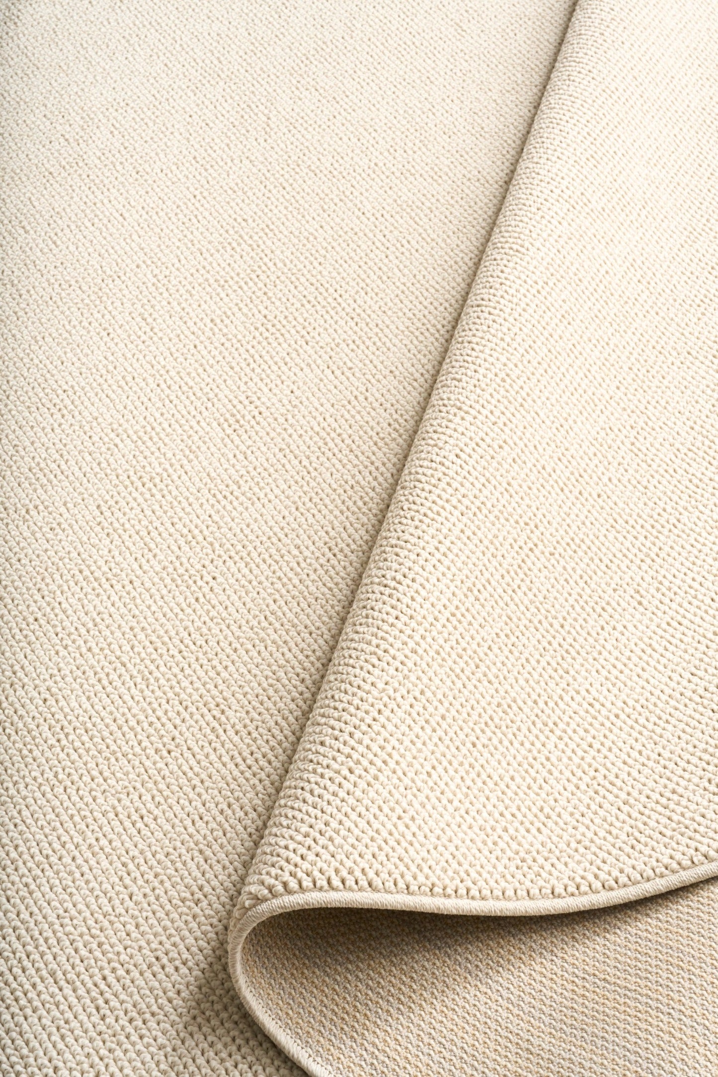 Cream woven area rug corner with rolled edge and fine loop texture