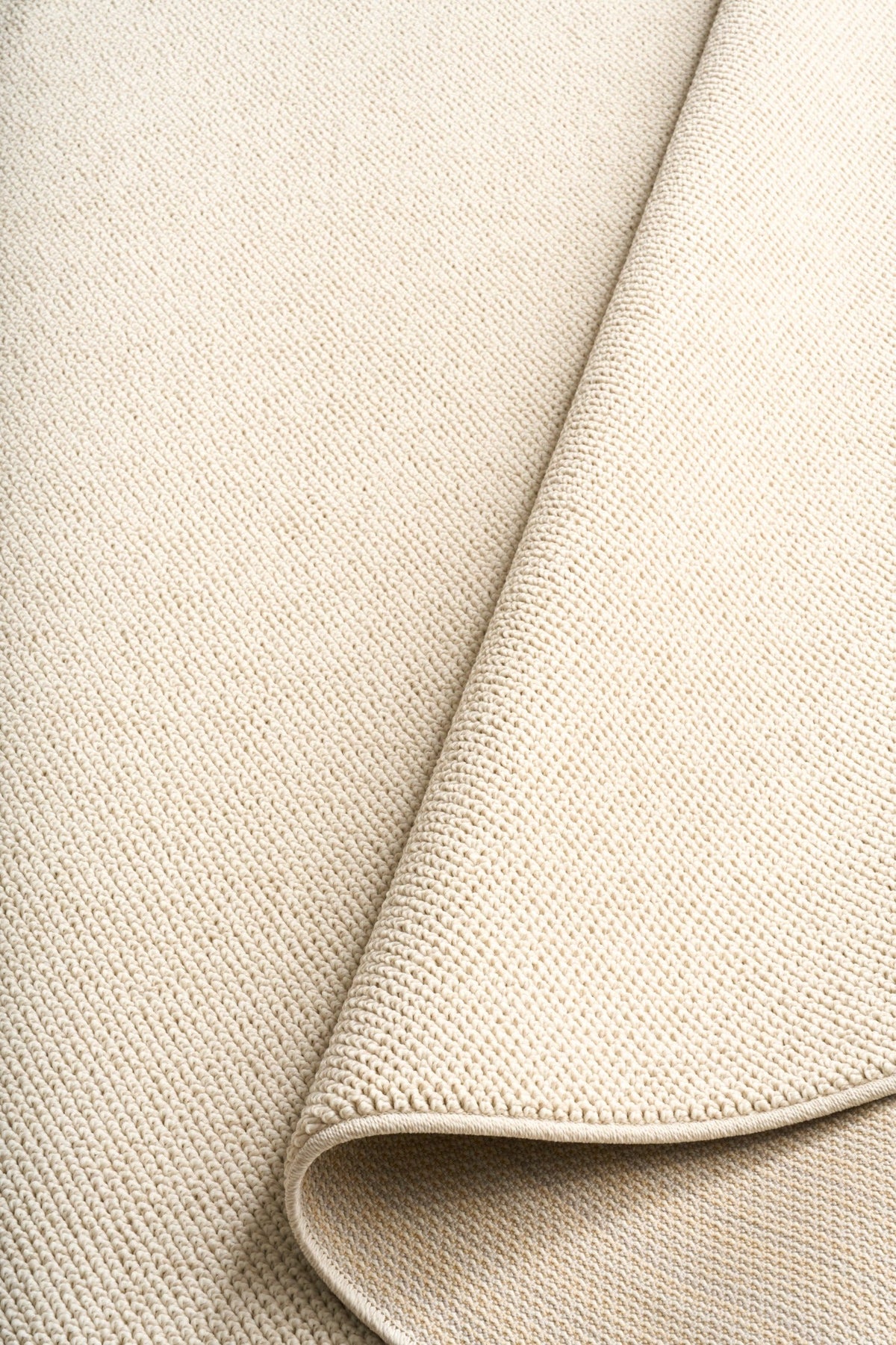 Cream woven area rug corner with rolled edge and fine loop texture