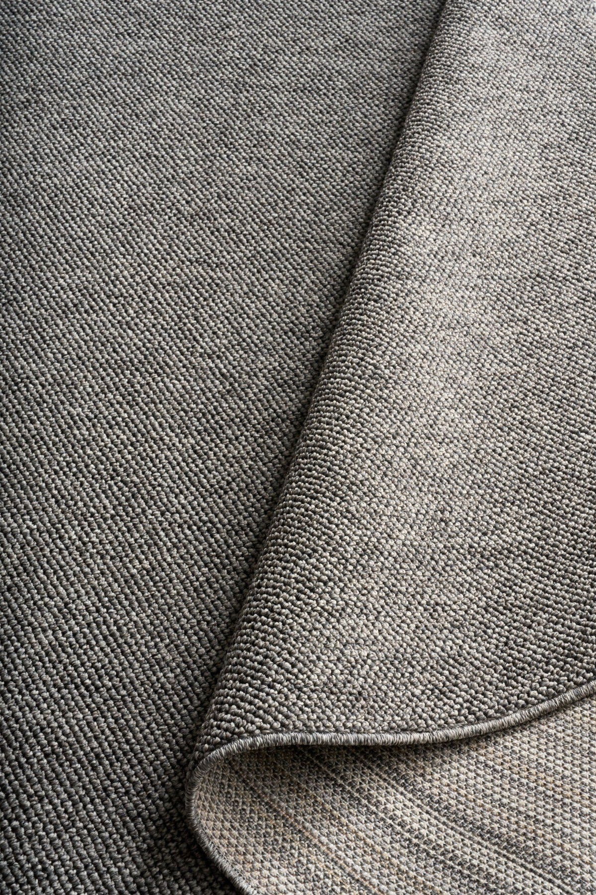 Grey woven area rug with stitched binding detail along the edge