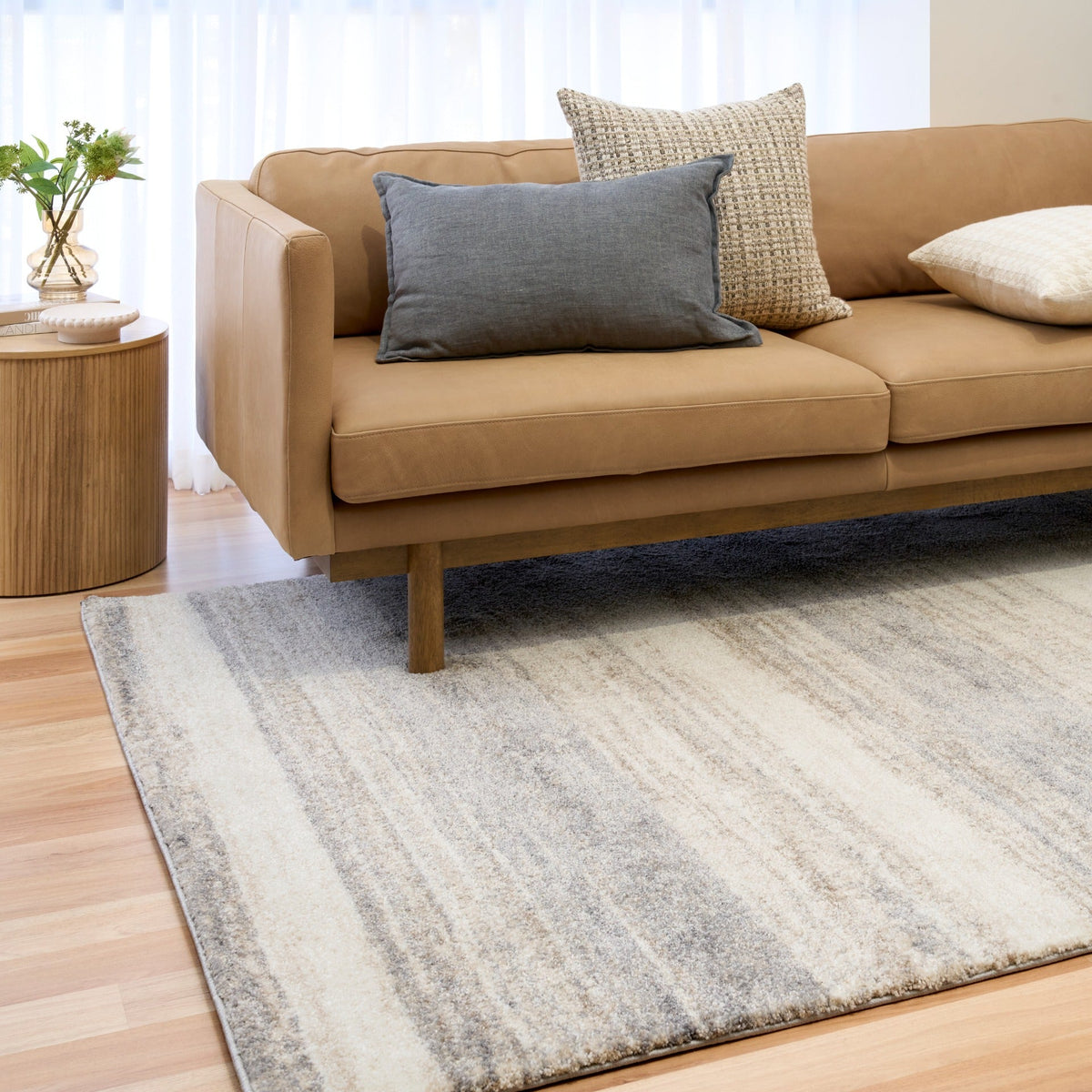 Bone grey horizontal striped area rug under a sofa on hardwood floor