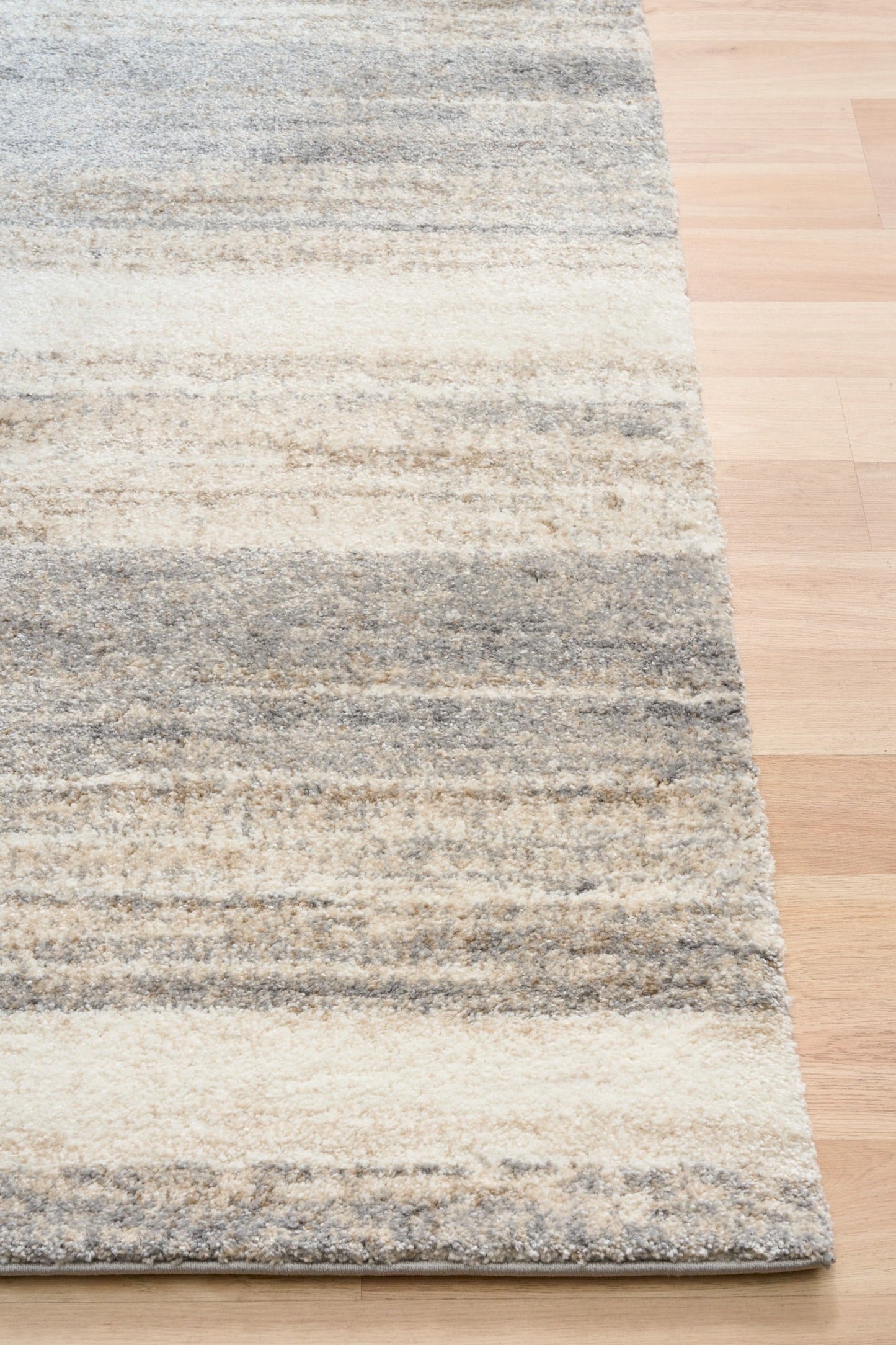 Bone grey striped area rug corner with bound edge on hardwood floor