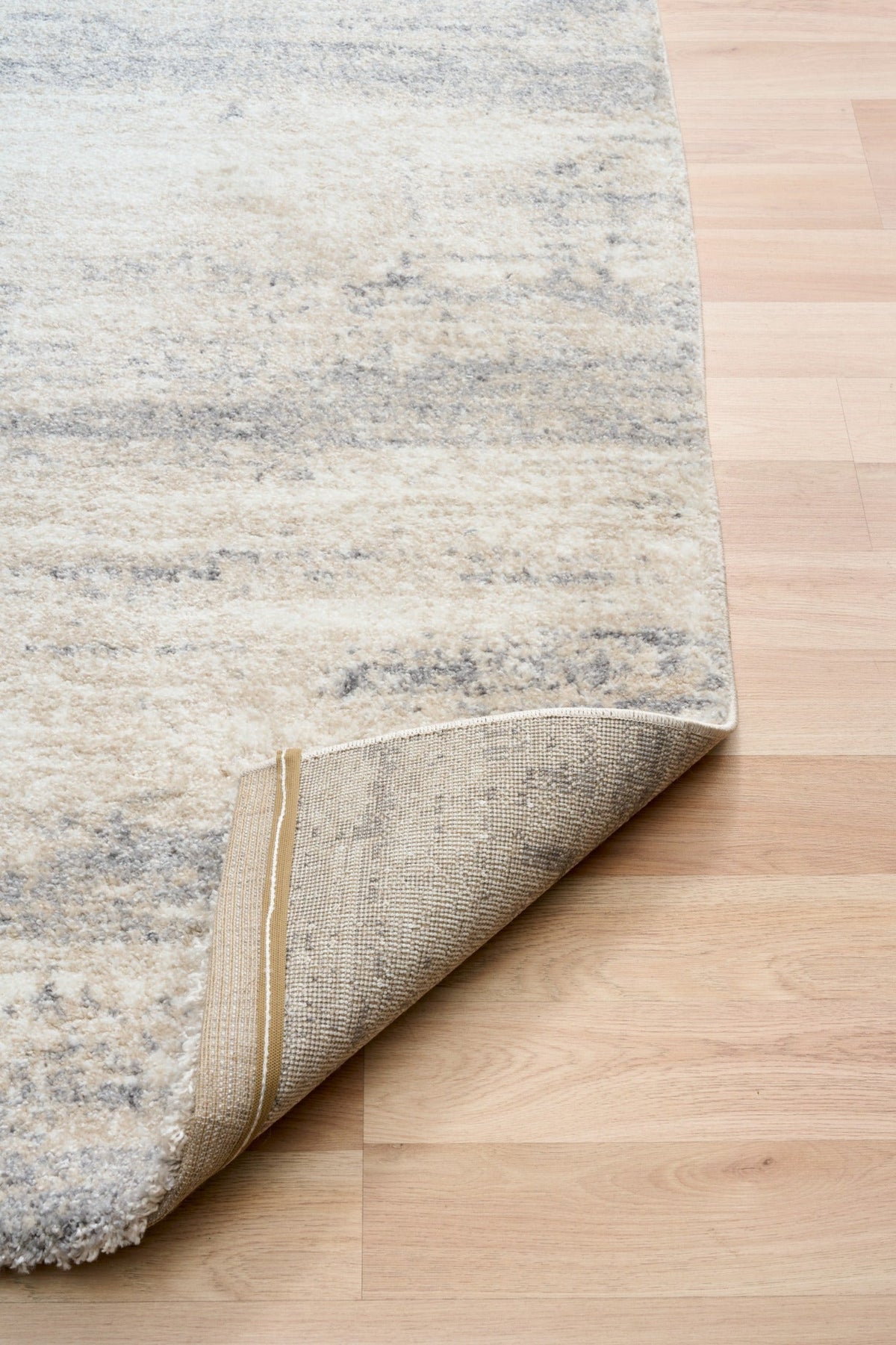 Grey and cream abstract area rug rolled back corner, showing short textured pile