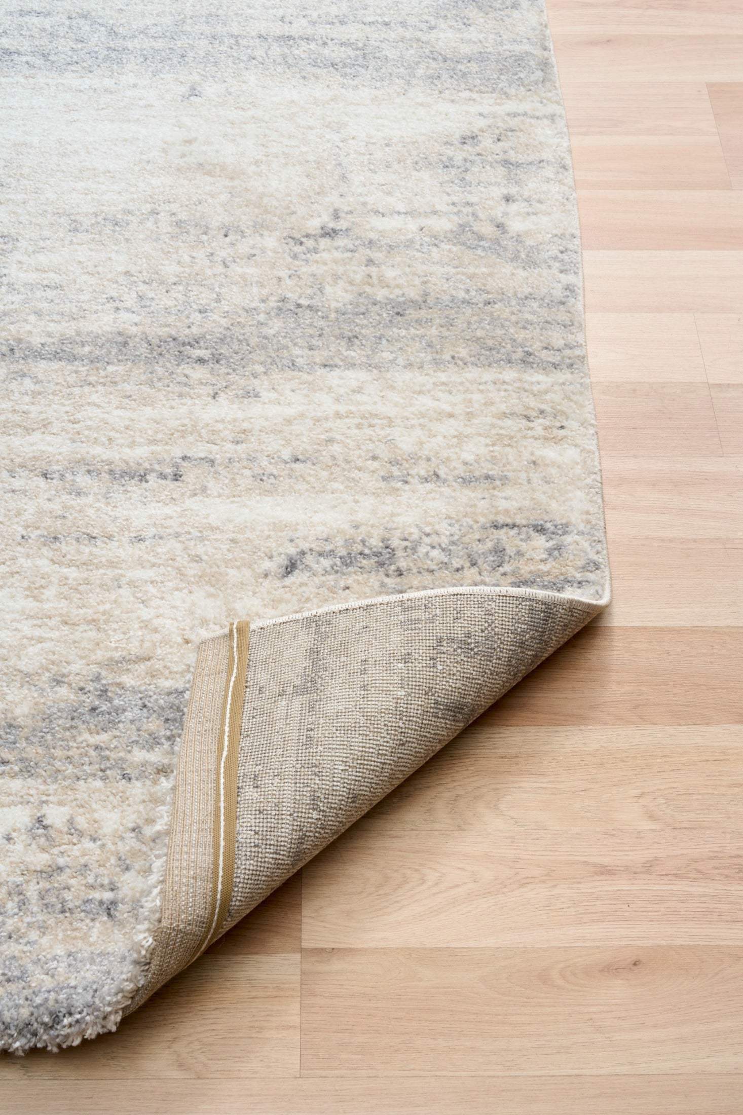 Grey and cream abstract area rug rolled back corner, showing short textured pile