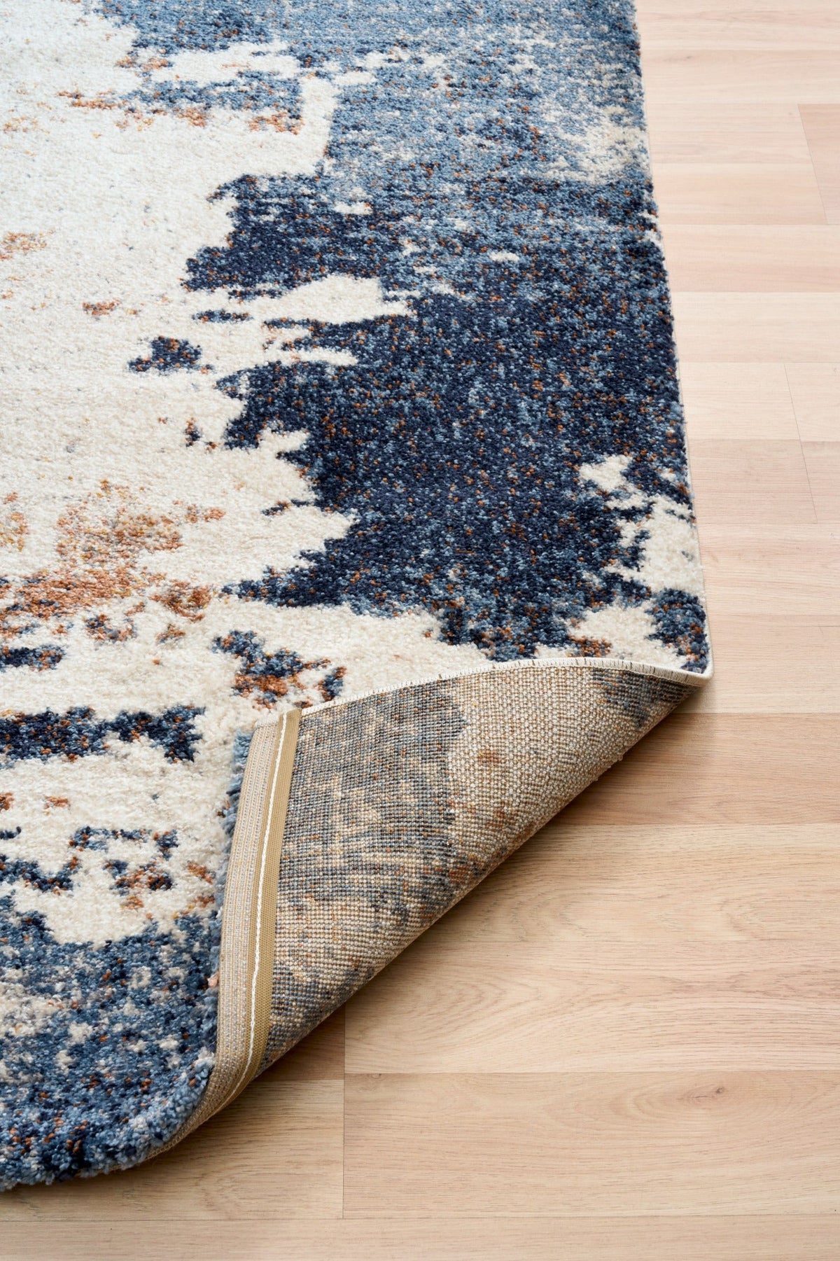 Corner view of rectangular rug with cream and blue distressed pattern; woven backing visible