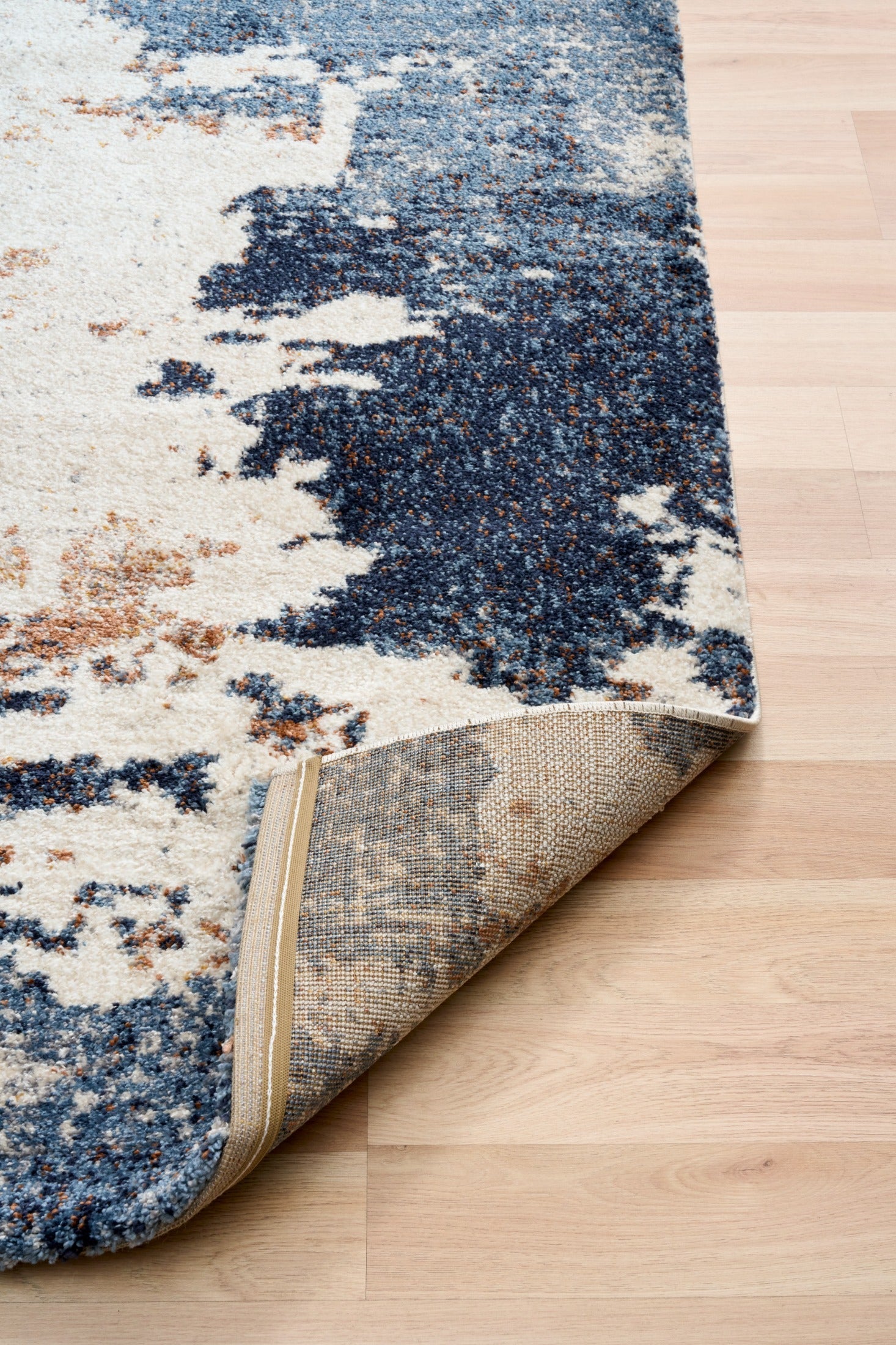 Corner view of rectangular rug with cream and blue distressed pattern; woven backing visible