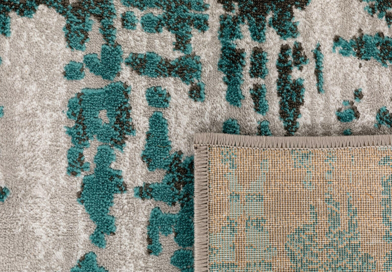 Corner detail of abstract rug with teal pattern and light woven edge backing
