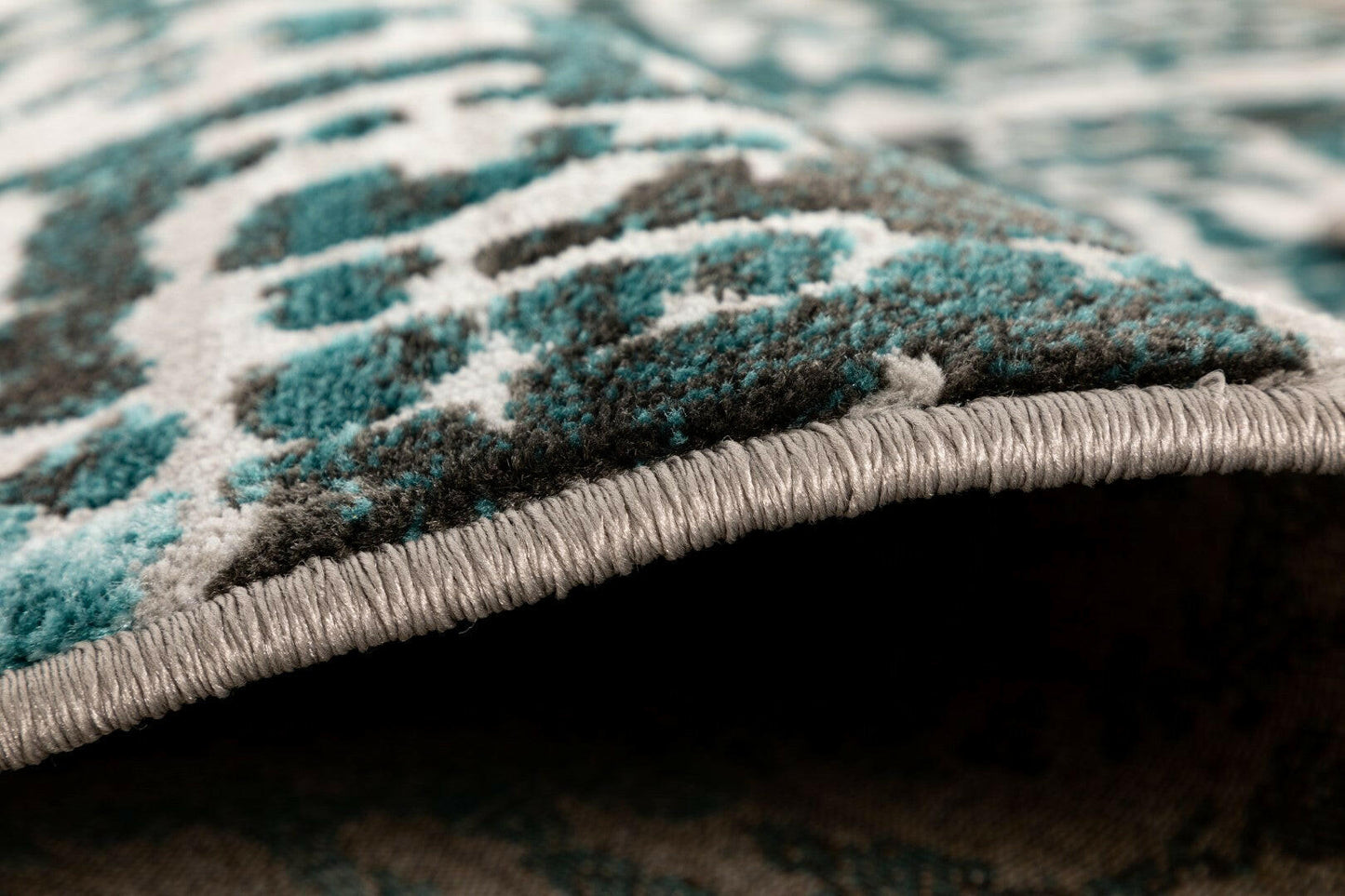 Close-up of textured abstract floor rug with teal pattern and gray bound edge