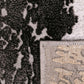 Corner of gray and white abstract rug with woven border and textured backing