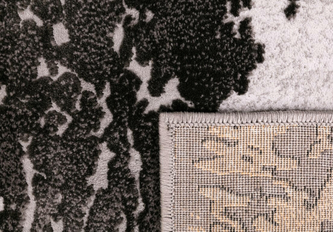 Corner of gray and white abstract rug with woven border and textured backing