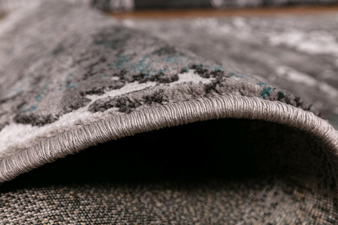 Rolled edge of gray and white area rug with thick textured pile and trim