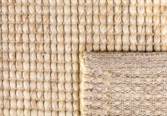 Beige wool rug corner with dense loop texture and contrasting woven edge border