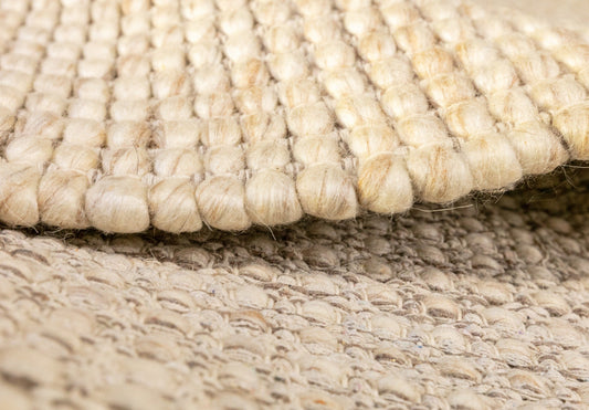 Beige wool rug edge with loop pile detail and layered backing along the border