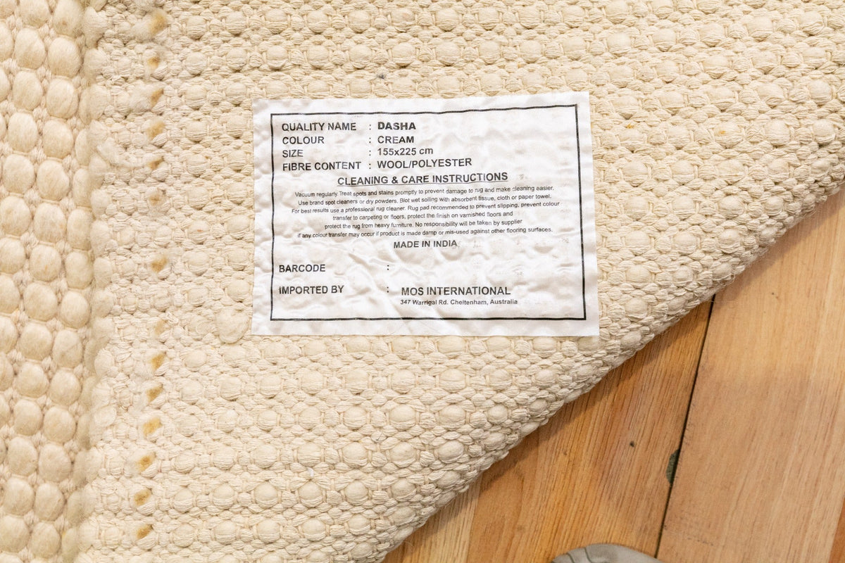 Cream wool rug corner with woven pile and small fabric label tag on underside