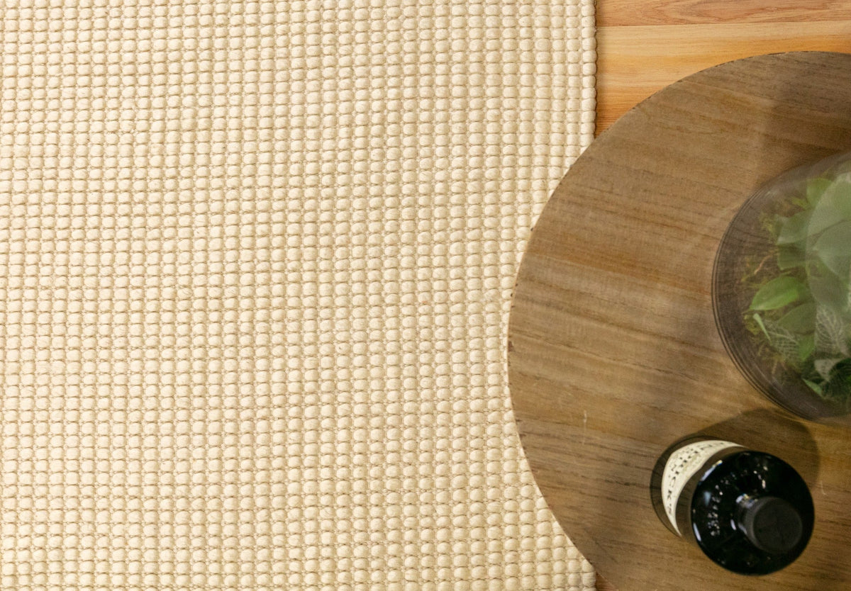 Cream wool rug corner with tightly woven, textured surface and looped fibers